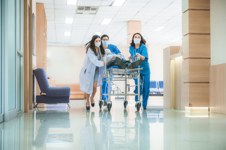 Emergency department, doctors and surgeons team move seriously injured patient lying on a stretcher through hospital corridors